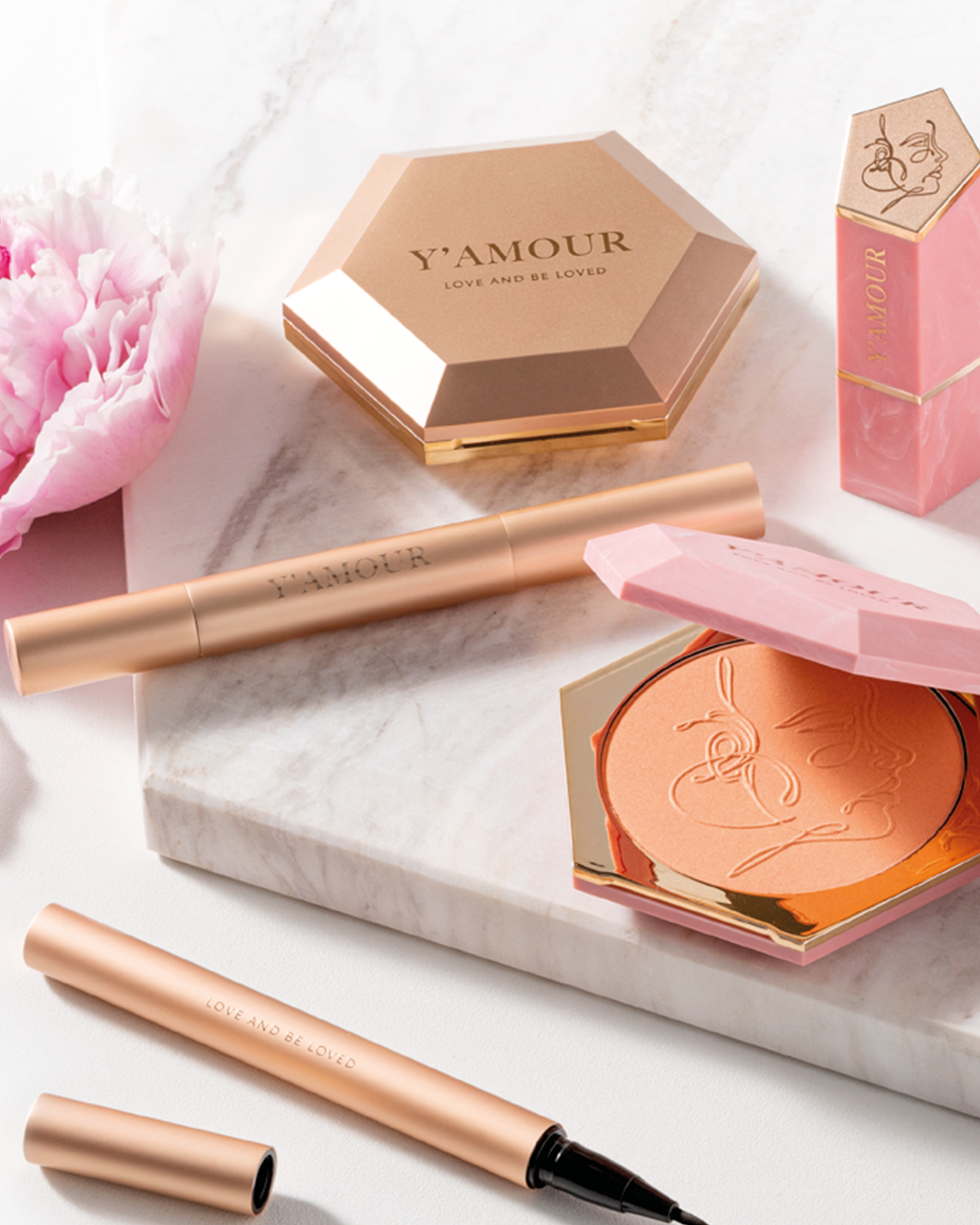 אוסף קוסמטיקה של יאמור מונח באופן אלגנטי על שטח מרמר, כולל קונטור נוזלי, קומפקט איפור ושפתון בסידור הרמוני